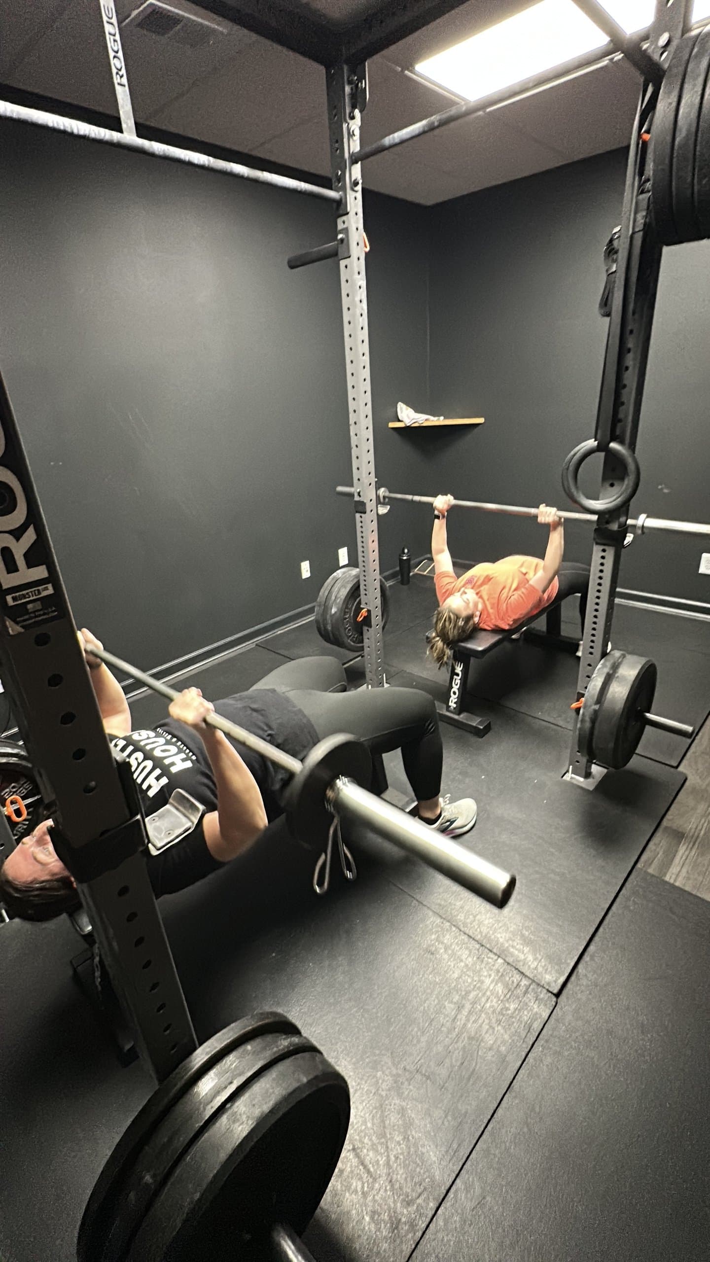 Two members bench pressing under coach supervision at Hustle House Health & Wellness in Woodstock, GA
