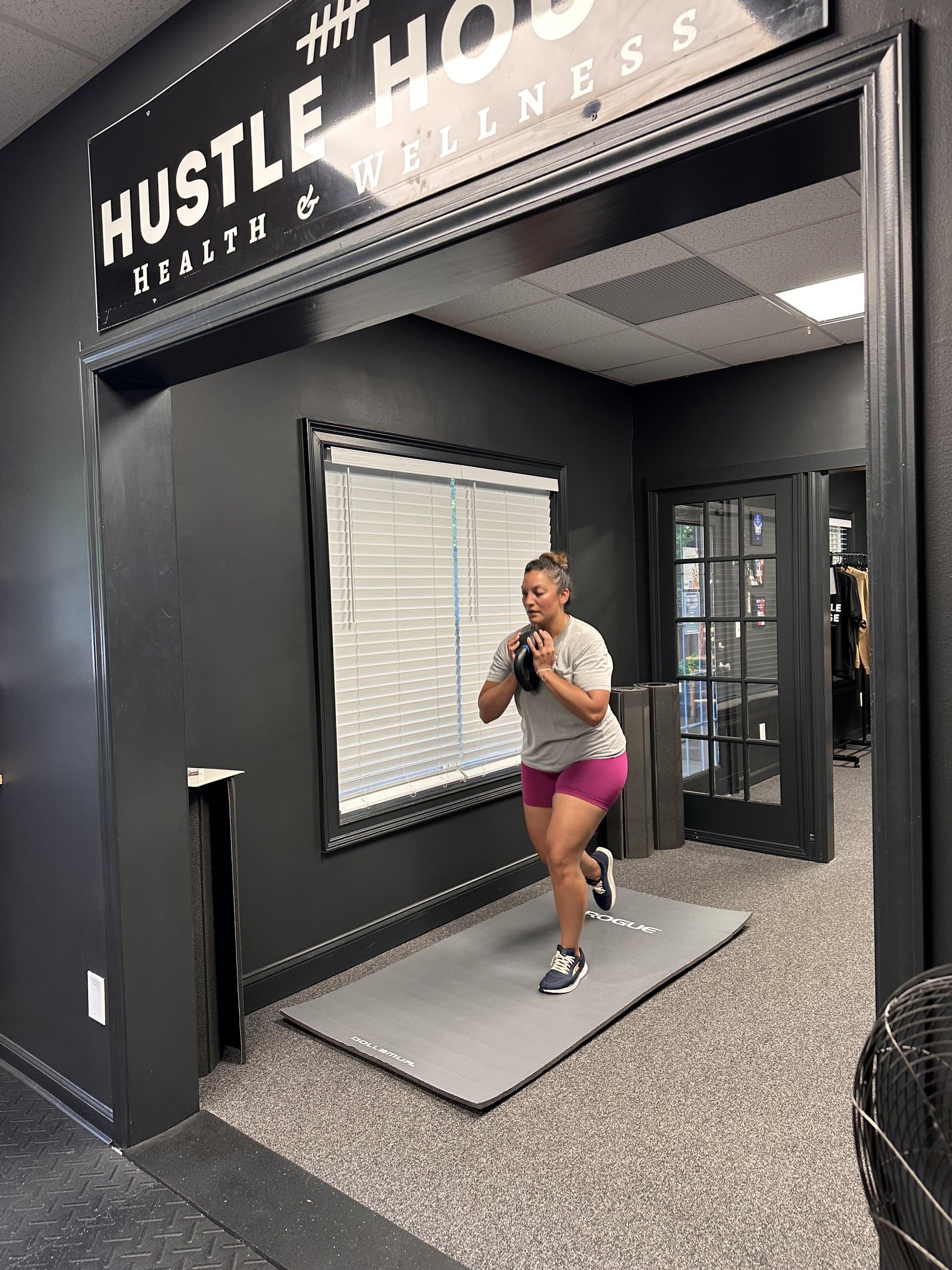 A member performing a kettlebell exercise at the studio entrance at Hustle House Health & Wellness in Woodstock, GA