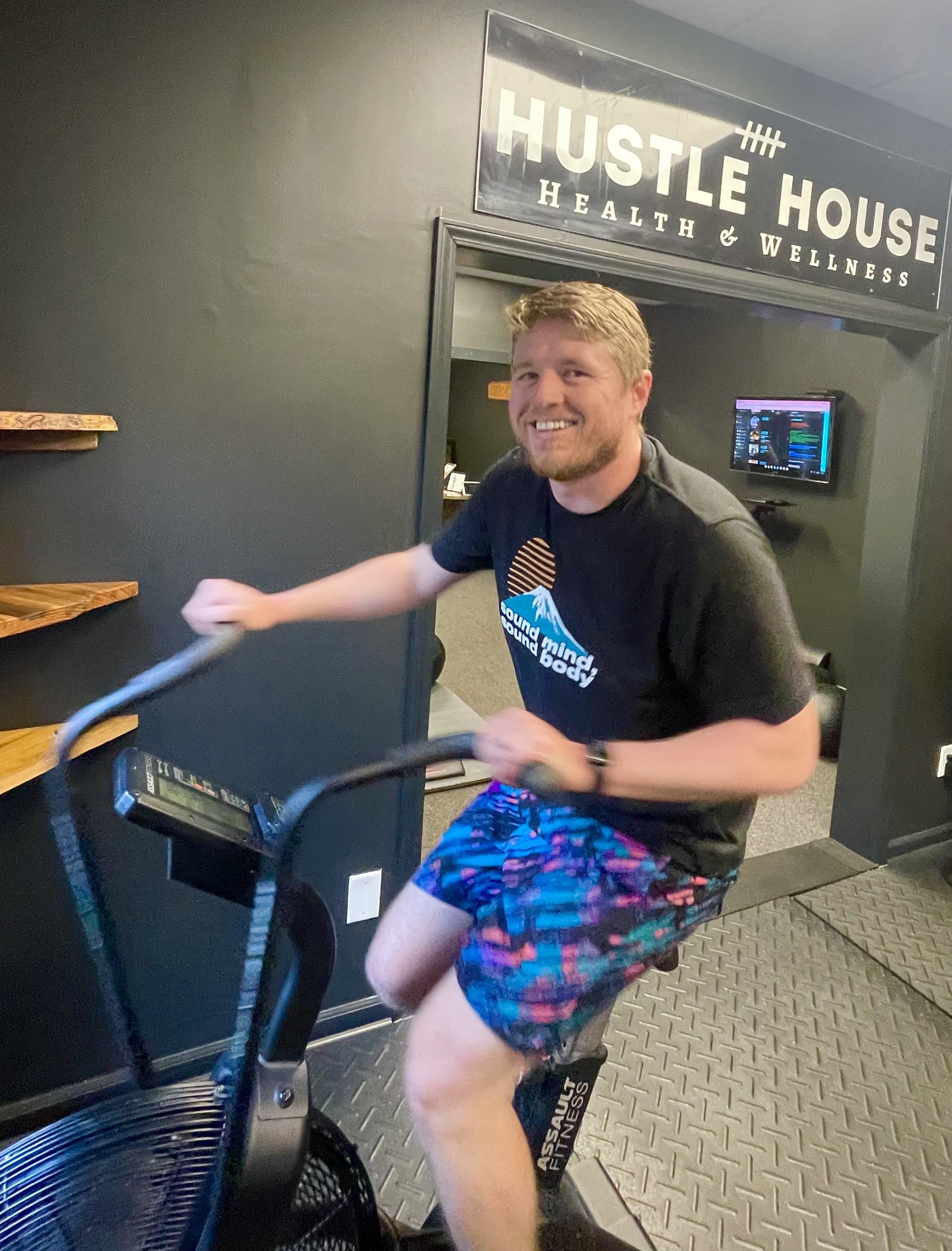 A member riding an air bike near the studio entrance at Hustle House Health & Wellness in Woodstock, GA