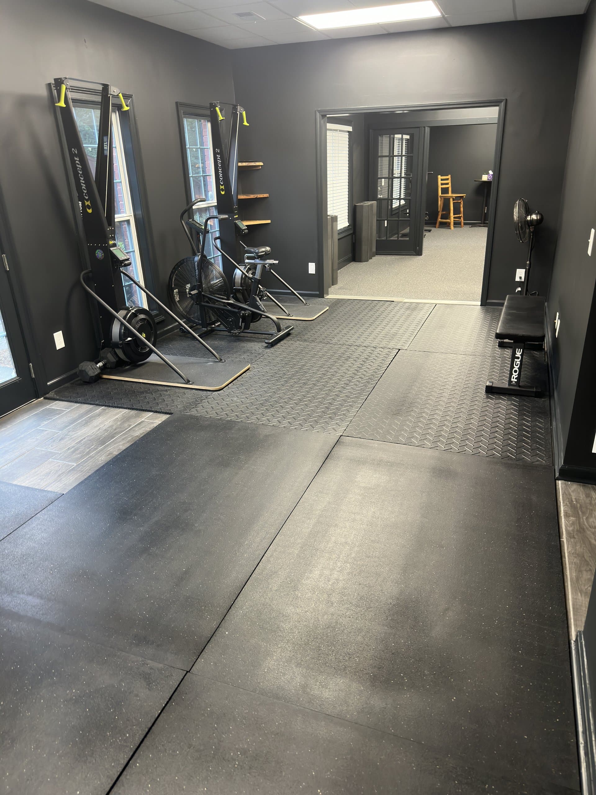 Air bikes and a weight bench on the rubber training floor at Hustle House Health & Wellness in Woodstock, GA